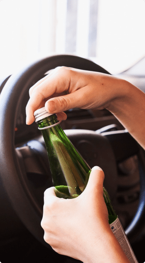 A man opening a beer bottle behind the steering wheel