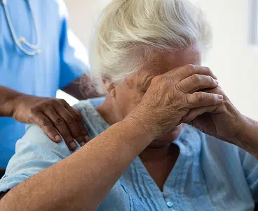 Elderly woman with hands folded on face