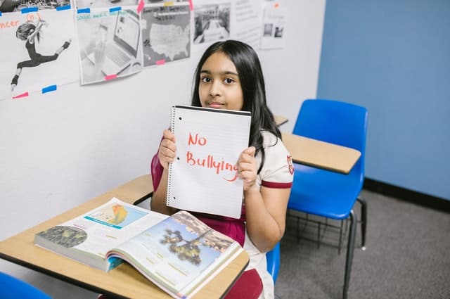 girl holding up a sign for "no bullying" in classroom